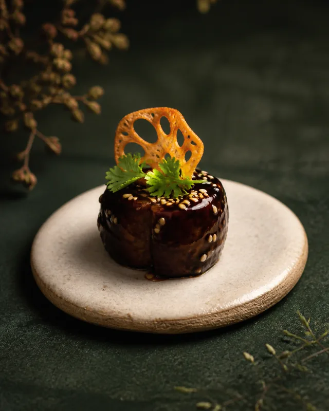 A glazed eggplant miso bite with sesame and a crisp lotus chip